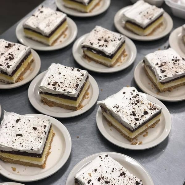 Multiple square dessert slices with white frosting and chocolate shavings on small plates.
