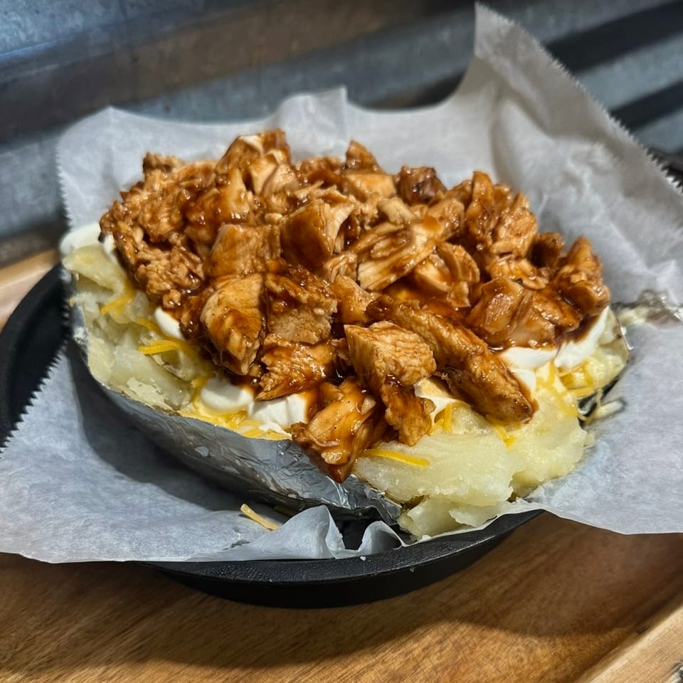 Baked potato topped with BBQ chicken, sour cream, and shredded cheese, served on parchment paper.