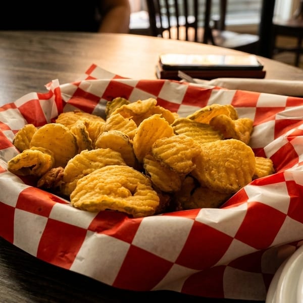 A basket of crispy fried pickles in a red and white checkered liner on a wooden table.