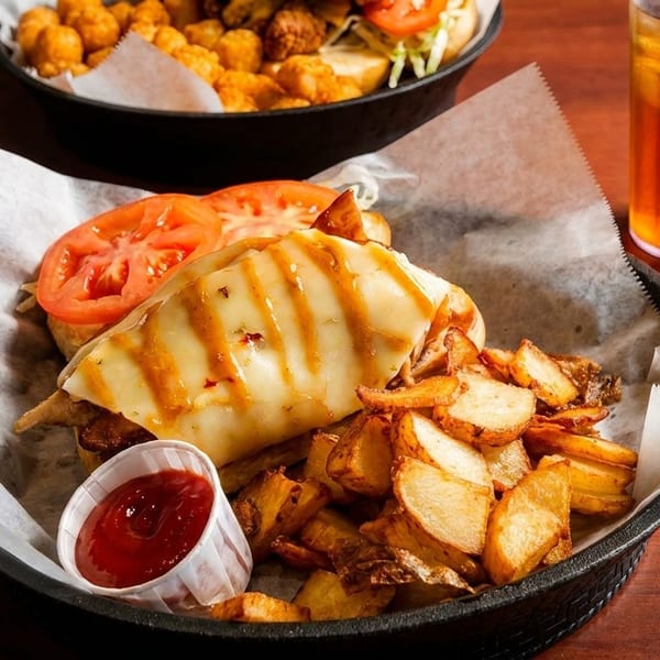 A grilled chicken sandwich with melted cheese, tomatoes, and a side of fries and ketchup.